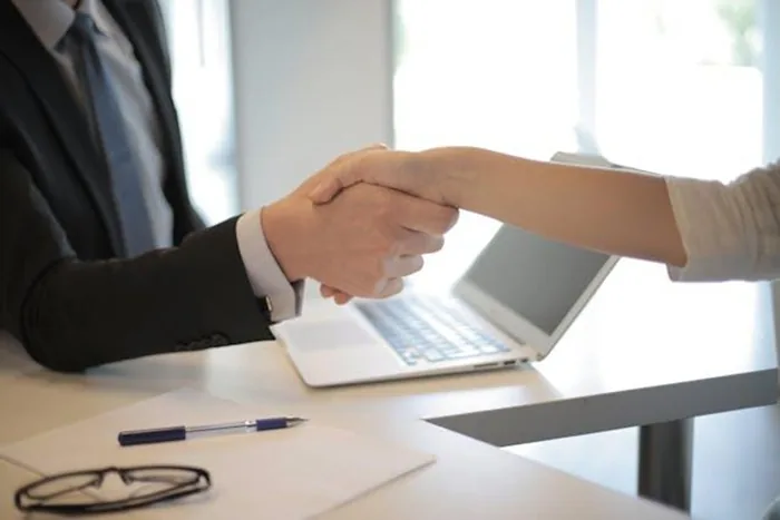 two people shaking hands over a computer